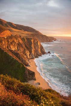 the beach is next to some cliffs near the ocean and mountains at sunset or sunrise