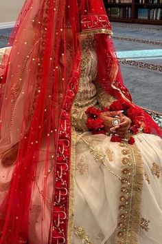 a woman in a red and white bridal gown sitting on the ground with her veil draped over her head