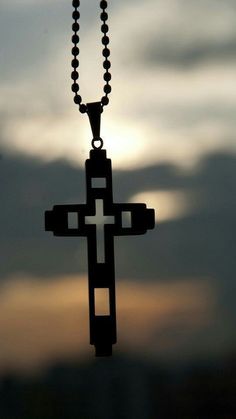 the silhouette of a cross on a chain is seen against a cloudy sky at sunset