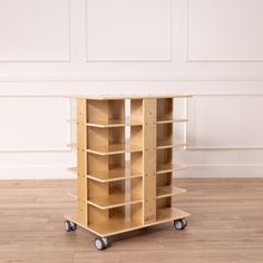 an empty wooden shelf on wheels in front of a white wall and hardwood flooring