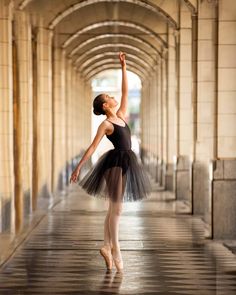 a young ballerina is standing in the middle of an empty hallway with her arms up