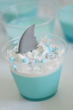 a shark fin is sticking out of the top of a cup filled with white and blue frosting