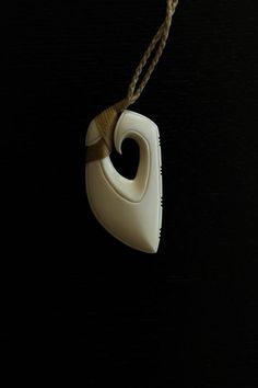 a white ceramic object hanging from a string on a black background with a brown cord