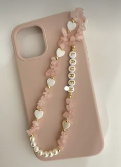 a pink phone case with some pearls and beads on the front, along with a gold beaded necklace