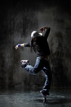 a man is dancing in the dark with his arms out and legs spread wide as he jumps