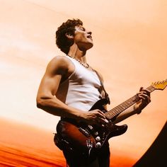 a man is playing an electric guitar in front of a bright orange background with his eyes closed