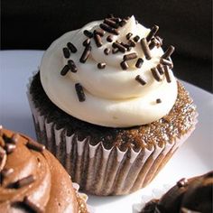 three chocolate cupcakes with white frosting and sprinkles on a plate