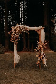 a wedding arch with flowers on it in the middle of some grass and trees behind it