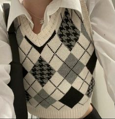 a woman wearing a white shirt and black and grey argyle sweater vest with her hands in her pockets