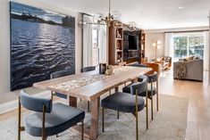 a dining room table with blue chairs in front of a large painting on the wall