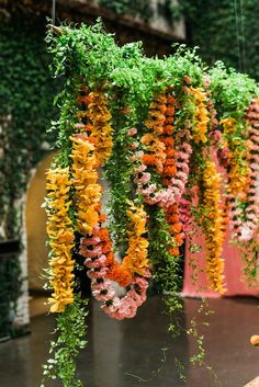 colorful flowers hanging from the ceiling in front of a wall covered with vines and greenery