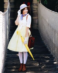 a woman in a yellow dress and hat is holding an umbrella while standing on a bridge