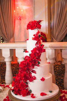 a white wedding cake with red flowers on the top and bottom, sitting on a table