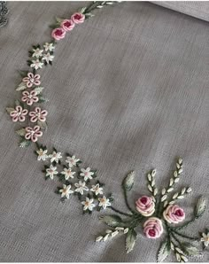 an embroidered necklace with pink flowers and green leaves on it, sitting on top of a gray cloth