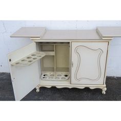 an antique white painted cabinet with two doors and shelves on the bottom, one door open