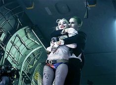 two people dressed as the joker and harley hugging each other in front of an airplane