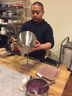 a man pouring something into a bowl on top of a wooden table