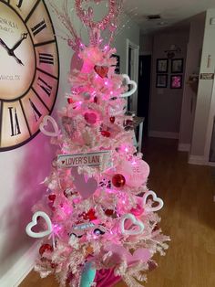 a pink christmas tree decorated with hearts and other decorations in front of a large clock