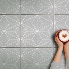 a woman holding a cup of coffee in front of a tiled wall