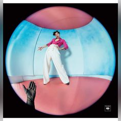 a woman in pink shirt and white pants standing next to a giant blue object with her hands on the ground