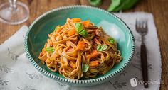 a bowl filled with pasta and vegetables on top of a table next to a glass of wine