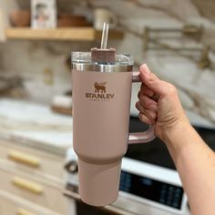 a person holding up a pink cup with a straw in it's mouth while standing next to an oven