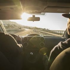 two people are driving down the road in their car and one person is wearing a hat