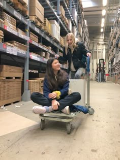 two women are sitting on a dolly in a warehouse and one is holding an apple