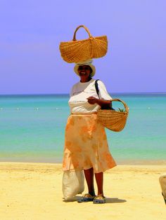 a woman standing on top of a sandy beach next to the ocean holding a basket