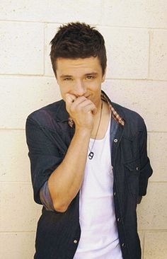 a young man leaning against a wall with his hand on his chin and looking at the camera