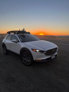 a white car parked on top of a dirt road next to the ocean at sunset