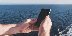 a person holding up a cell phone in their hand on the deck of a boat