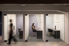 a woman sitting at a desk in an office cubicle with glass partitions on the walls