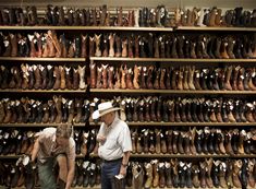 two people standing in front of a wall full of pairs of shoes and hats on display