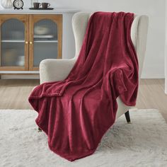 a white chair with a red blanket on it in front of a cabinet and clock