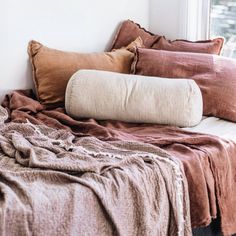 a bed with pillows and blankets on top of it next to a window sill