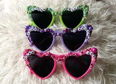 three pairs of heart shaped sunglasses with eyeballs and beads on the lenses are laying on a fluffy white surface