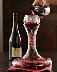 a person pouring red wine into a glass in front of two bottles on a table