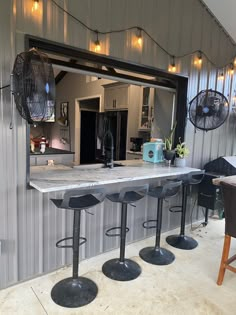 a bar with four stools in front of it and a fan hanging from the ceiling