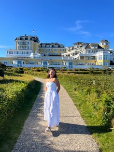 a woman in a white dress is standing on a path next to a large building