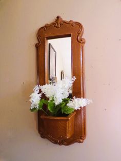 a mirror hanging on the side of a wall with flowers in it and a potted plant