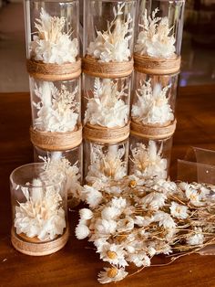 several clear vases filled with white flowers on top of a wooden table next to other glass containers