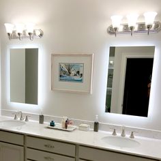 a bathroom with double sinks and two mirrors on the wall above them is lit up by three lights