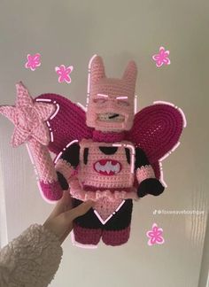 a person holding up a pink crocheted toy in front of a white wall