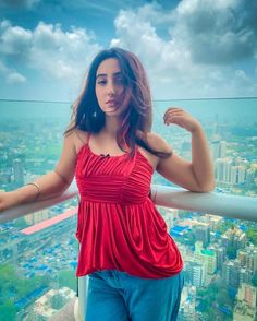 a woman standing on top of a building with her arms behind her head and looking at the camera