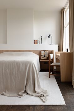 a bed with a white blanket on top of it next to a desk and chair