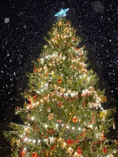 a large christmas tree with lights and decorations on it's branches in the snow