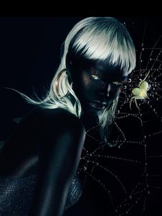 a woman with white hair and black makeup is holding a spider web in front of her face