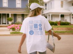 a woman walking down the street carrying a purse and wearing a t - shirt with images on it