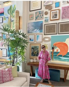 a woman standing in front of a living room filled with pictures and paintings on the wall